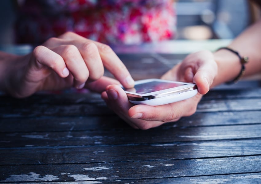 Women sitting at wooden table, using a smartphone