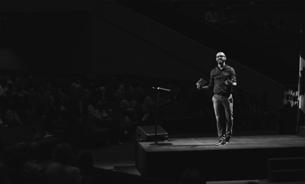 Black and white picture of man present on a stage to crowd